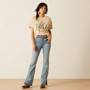 Woman wearing a beige t-shirt with a graphic design and light blue jeans against a plain background