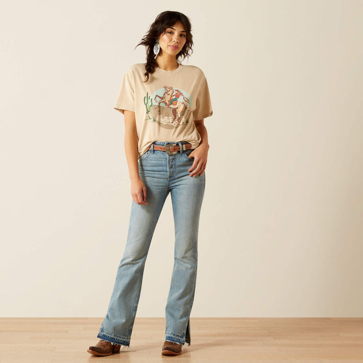 Woman wearing a beige t-shirt with a graphic design and light blue jeans against a plain background